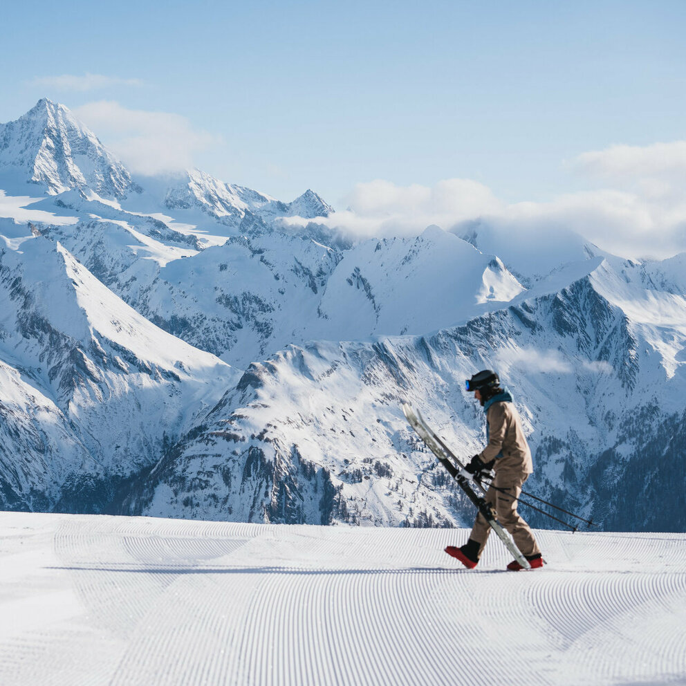 Winterliches Panorama mit dem Großglockner im Hintergrund und einem Skifahrer im Vordergrund, der sich gerade bereit macht, in seine Ski zu steigen.