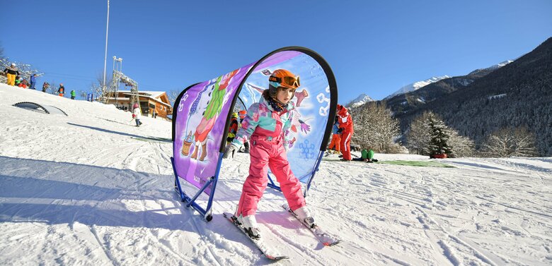 Ein Mädchen in rosa Skianzug fährt durch einen lila Tunnel im Familienskigebiet Virgen bei Kaiserwetter.