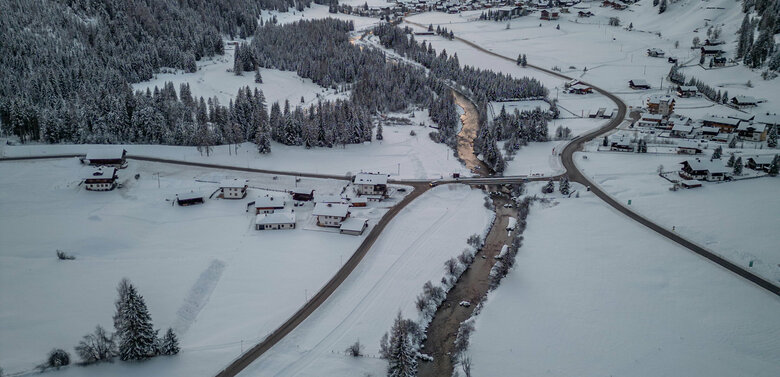 Das winterliche St. Jakob i. D. mit der talsauswärts fließenden Schwarzach, imposanten Bergen im Hintergrund und Abendrot am Himmel.