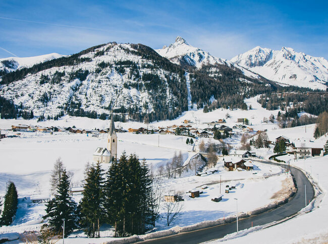 Blick auf das verschneite Kals mit Kirche und Wohnhäusern, an einem sonnigen Tag.