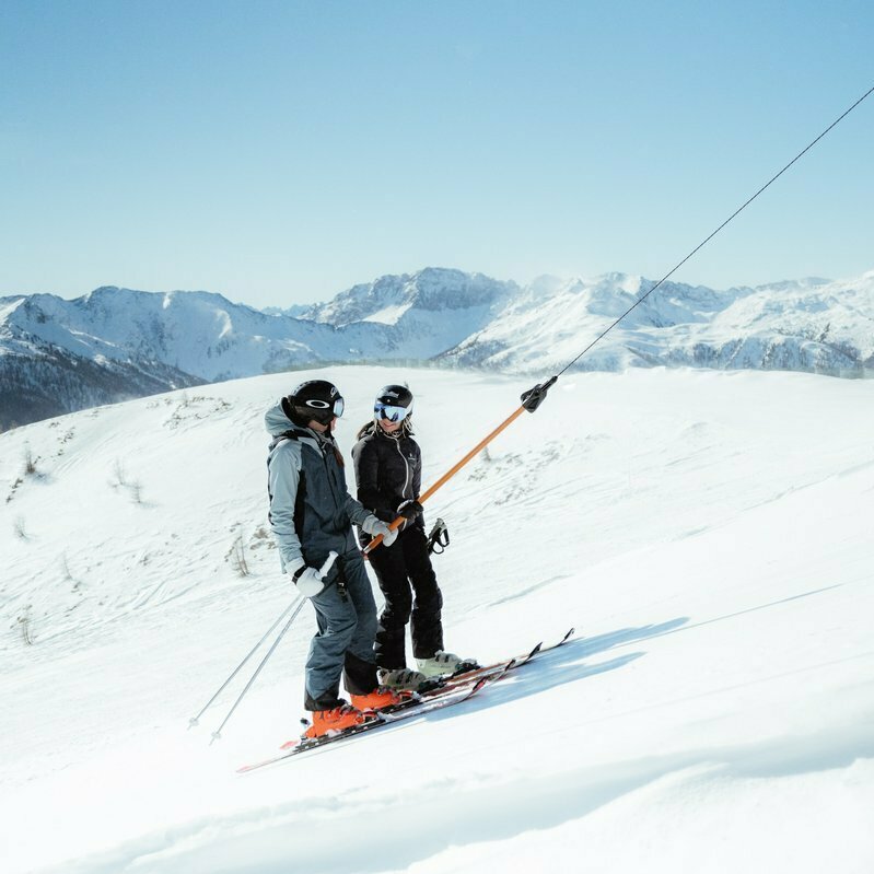Zwei Skifaher:innen lassen sich im Skigebiet Golzentipp in Obertilliach bei strahlendem Sonnenschein von einem Schlepplift auf den Berg ziehen