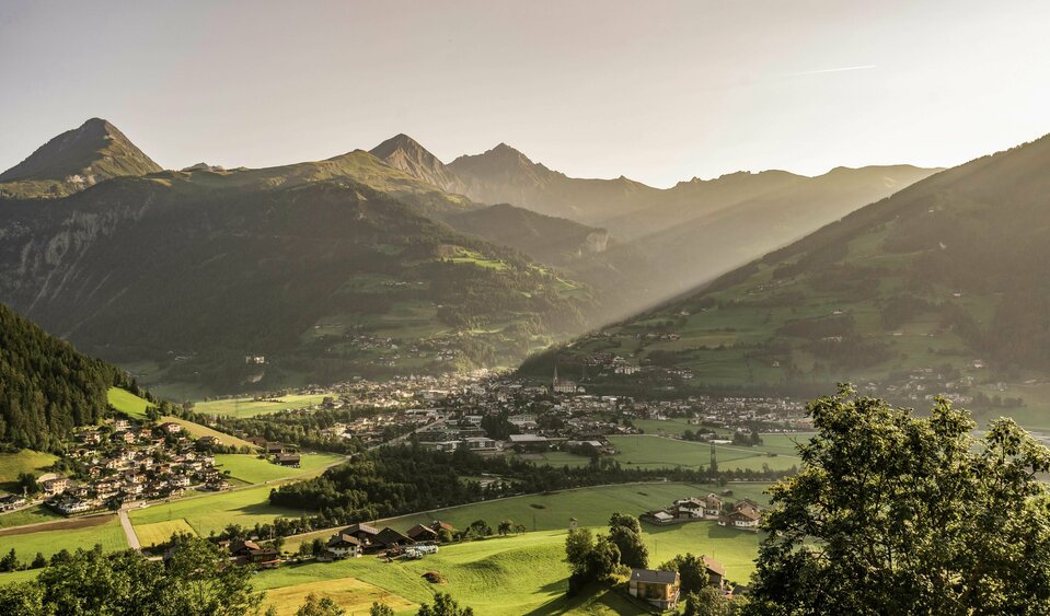 Blick auf die Gemeinde Matrei und die umliegende Berglandschaft. Die Sonne blitzt hinter den Bergen hervor.