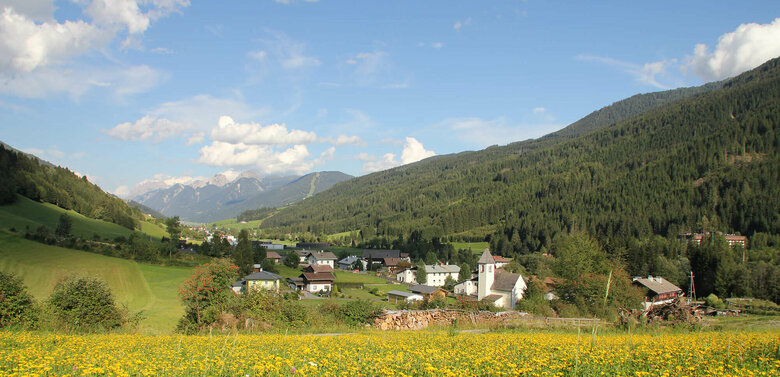Zu sehen ist die Ortschaft Arnbach mit einer blühenden Wiese im Vordergrund.