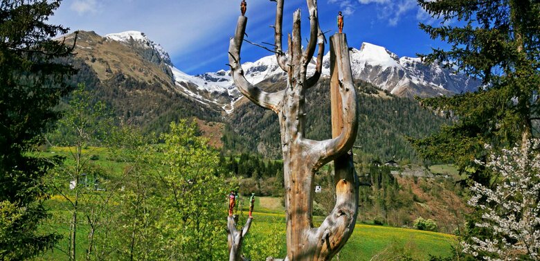 Eine hölzerne Figur im Skulpturenpark Virgen mit Bergpanorama im Hintergrund.