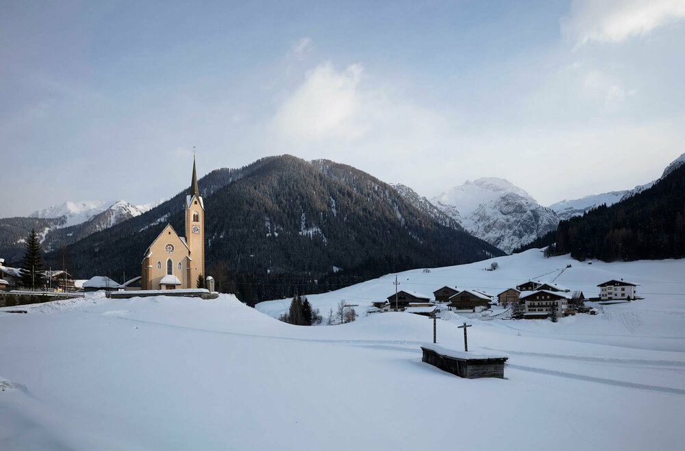 Kartitscher Pfarrkirche mit den sich dahinter erhebenden bewaldeten Hänge der Karnischen Alpen in tief winterlicher Stimmung