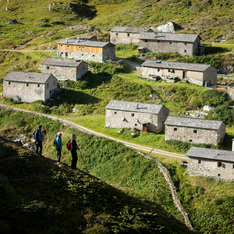 Drei Wanderer blicken auf die Steingebäude der Jagdhausalmen im Nationalpark Hohe Tauern.