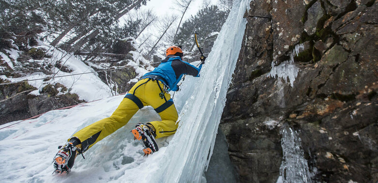 Eiskletterer klettert auf einem zugefrorenen Wasserfall senkrecht nach oben