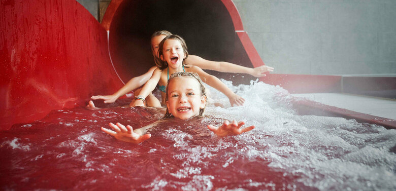 Drei Mädchen am Ausgang einer roten Wasserrutsche im Dolomitenbad in Lienz.
