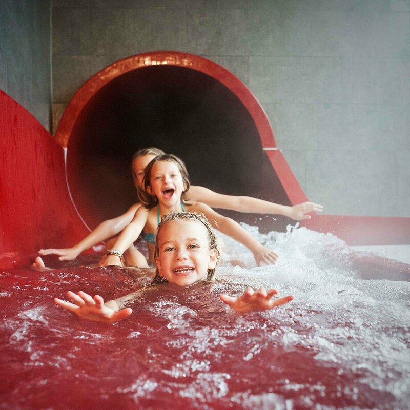 Drei Mädchen am Ausgang einer roten Wasserrutsche im Dolomitenbad in Lienz.