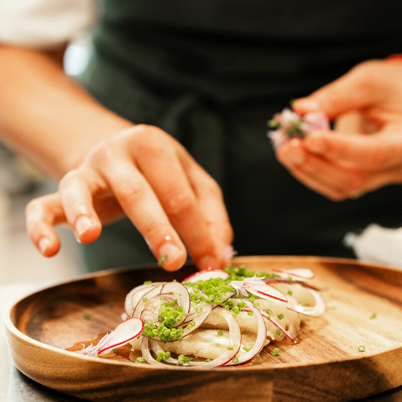 Köchin bereitet einen Holzeller mit Kräuter-Topfen-Ravioli vor.