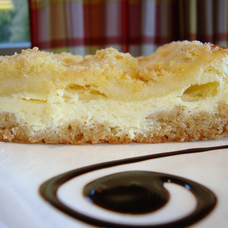 Ein Topfen-Streuselkuchen auf einem Teller mit Schoko-Soße verziert.