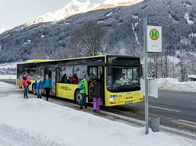 Gelber Bus hält an einer Bushaltestelle im Winter und lässt Fahrgäste ein- und aussteigen.