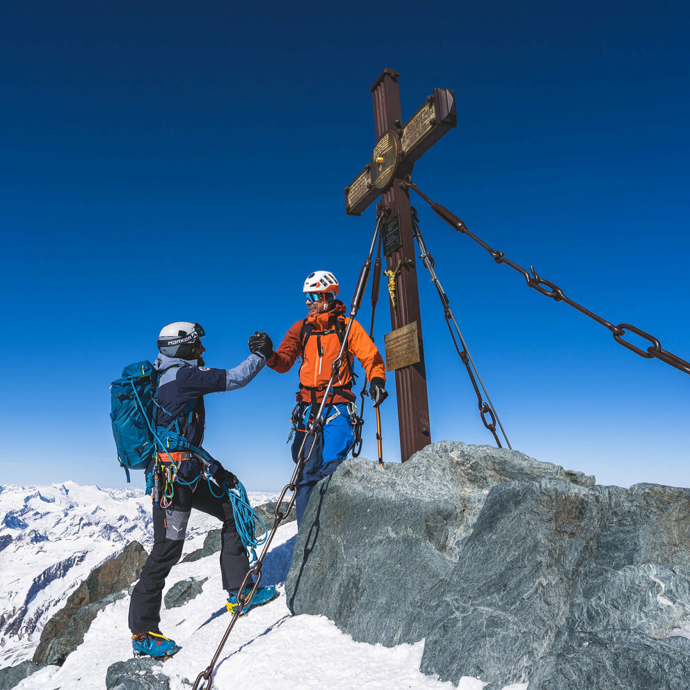 Zwei Skitourengeher:innen erreichen das Gipfelkreuz des Großglockners