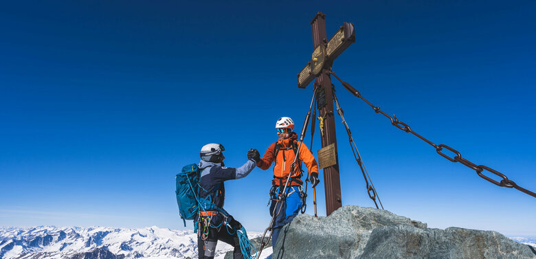 Zwei Skitourengeher:innen erreichen das Gipfelkreuz des Großglockners