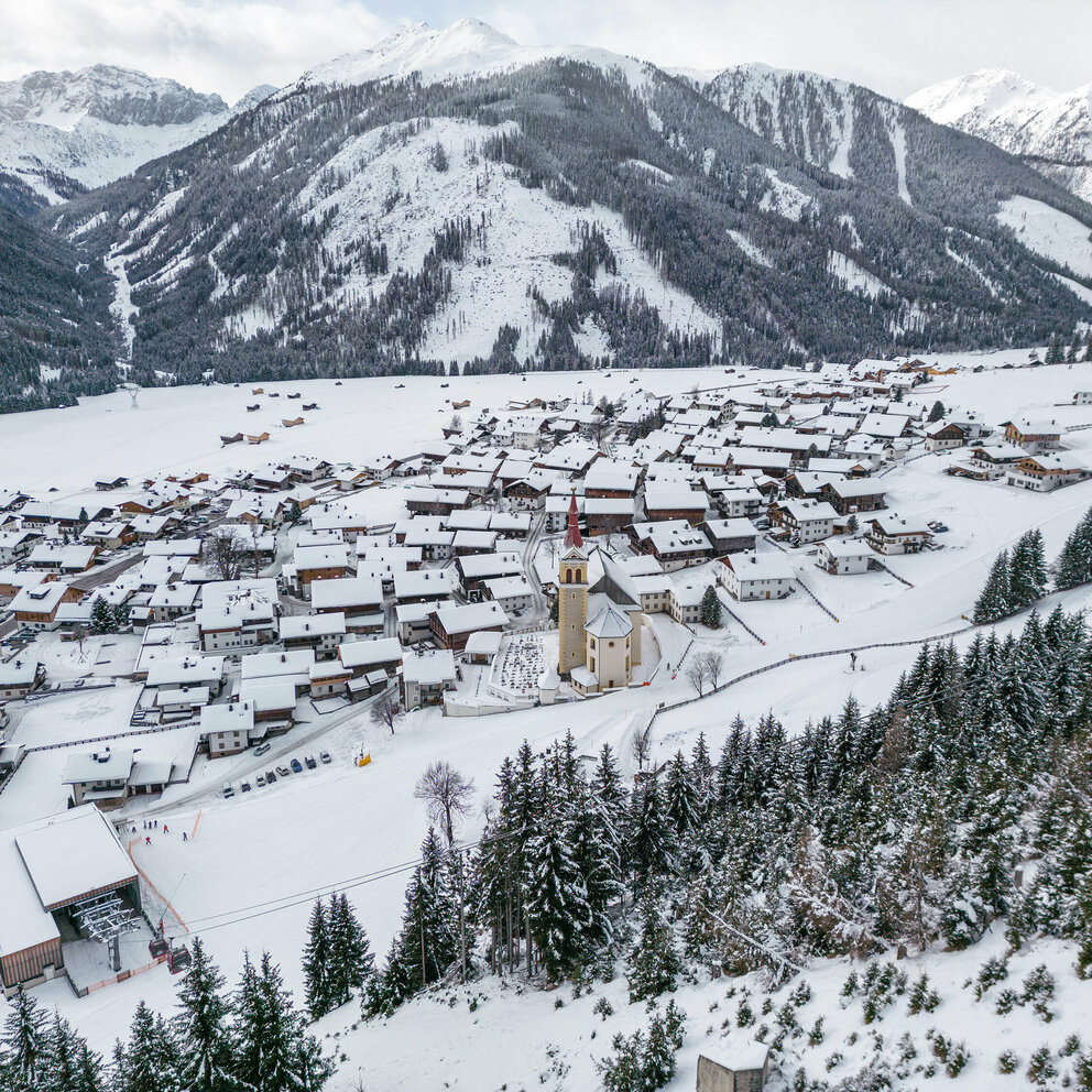 Blick auf den Schwemmkegel mit den eng beieinander stehenden Häusern im verschneiten Obertilliach von der Gondel aus bei der Bergfahrt.