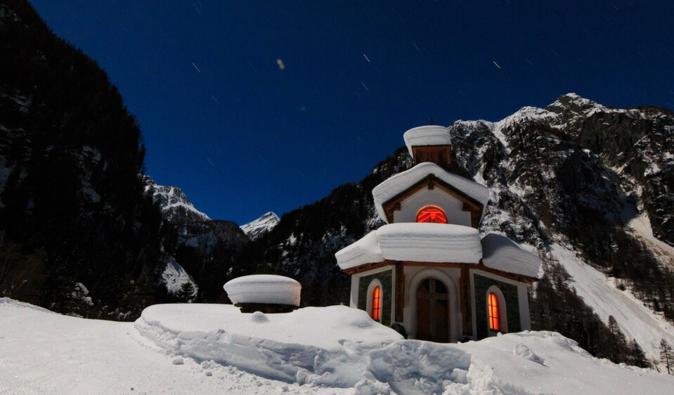 Die schneebedeckte, beleuchtete Hubertuskapelle in Ströden in der Dämmerung.