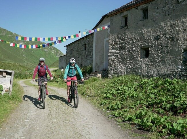 Zwei Radfahrer fahren auf einem Schotterweg vorbei an den Jagdhausalmen.