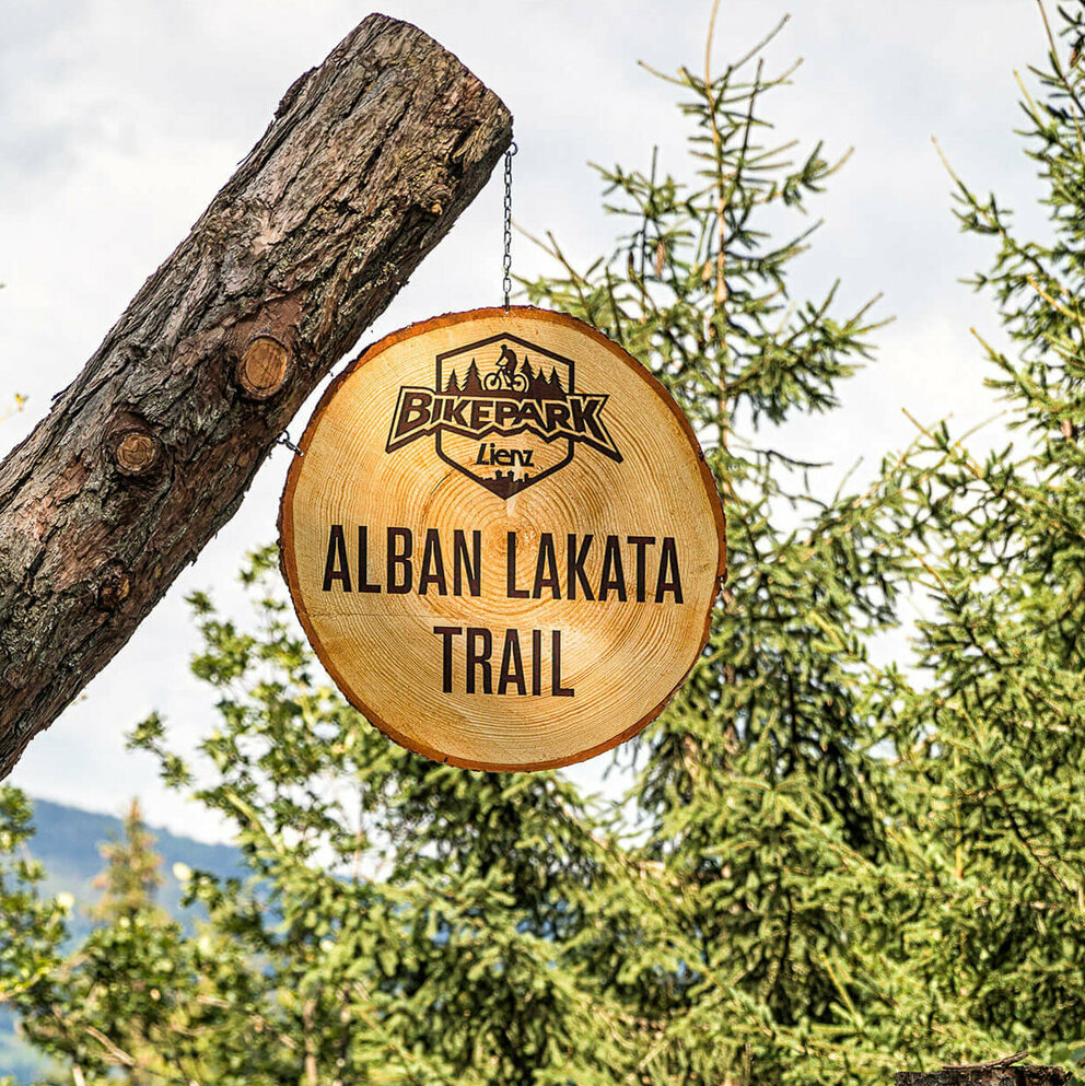 Zwei Radfahrer mit roter Bekleidung und gelben Helmen am Eingang des Alban Lakata Trails im Bikepark Lienz.
