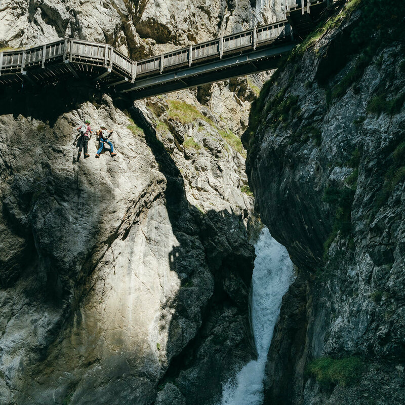 Galitzenklamm Klettersteig Zwei Personen auf dem Klettersteig in der Galitzenklamm. Sie befinden sich unterhalb des hölzernen Weges und neben einem Wasserfall.