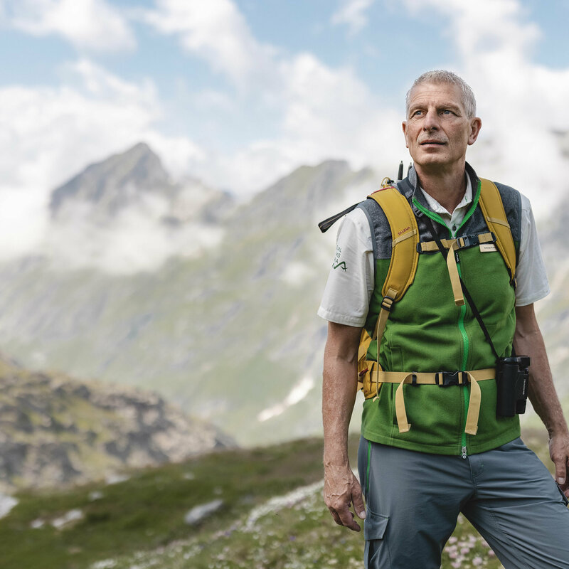 Ein Ranger des Nationalpark Hohe Tauern mit grüner Weste steht im Gschloesstal und blickt in die Bergwelt.