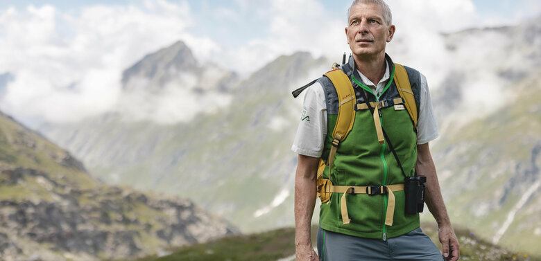 Ein Ranger des Nationalpark Hohe Tauern mit grüner Weste steht im Gschloesstal und blickt in die Bergwelt.