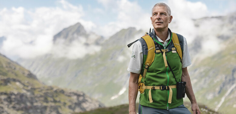 Ein Ranger des Nationalpark Hohe Tauern mit grüner Weste steht im Gschloesstal und blickt in die Bergwelt.