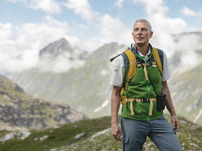 Ein Ranger des Nationalpark Hohe Tauern mit grüner Weste steht im Gschloesstal und blickt in die Bergwelt.