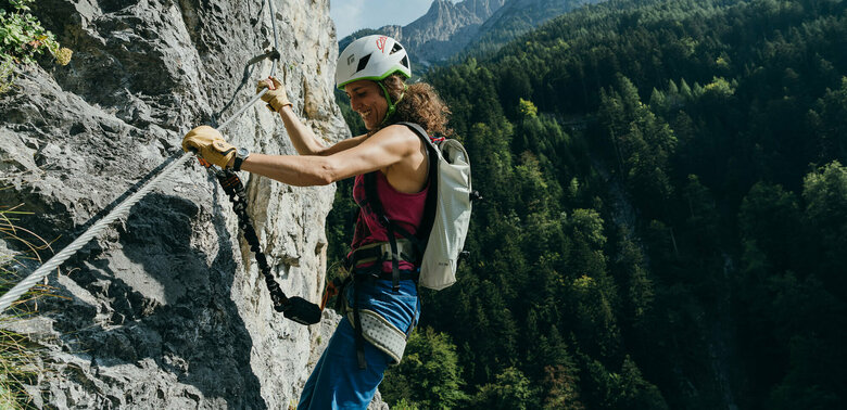 Galitzenklamm Klettersteig Eine Frau mit Helm und Rucksack hängt mit Kletterausrüstung im Galitzenklamm Klettersteig.