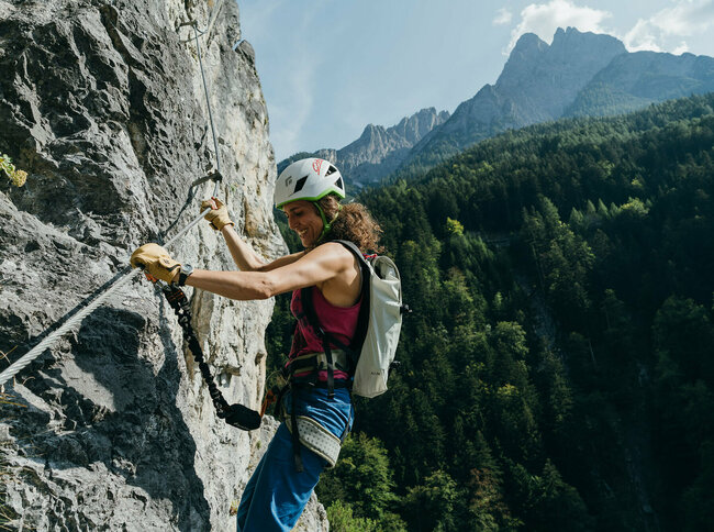 Eine Frau mit Helm und Rucksack hängt mit Kletterausrüstung im Galitzenklamm Klettersteig.