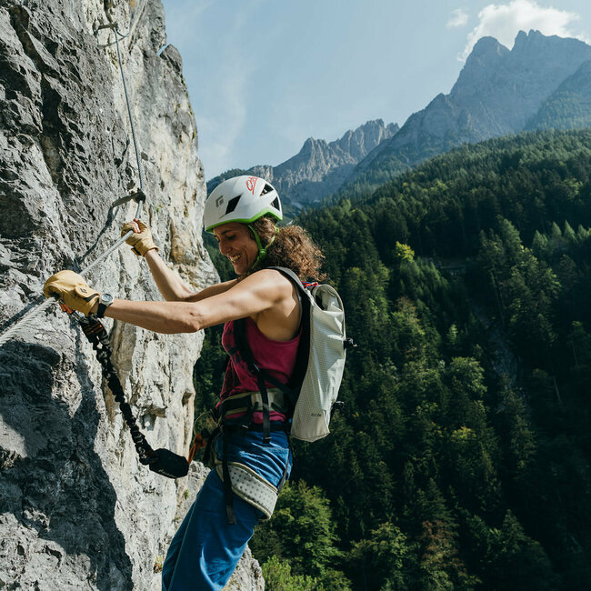 Eine Frau mit Helm und Rucksack hängt mit Kletterausrüstung im Galitzenklamm Klettersteig.