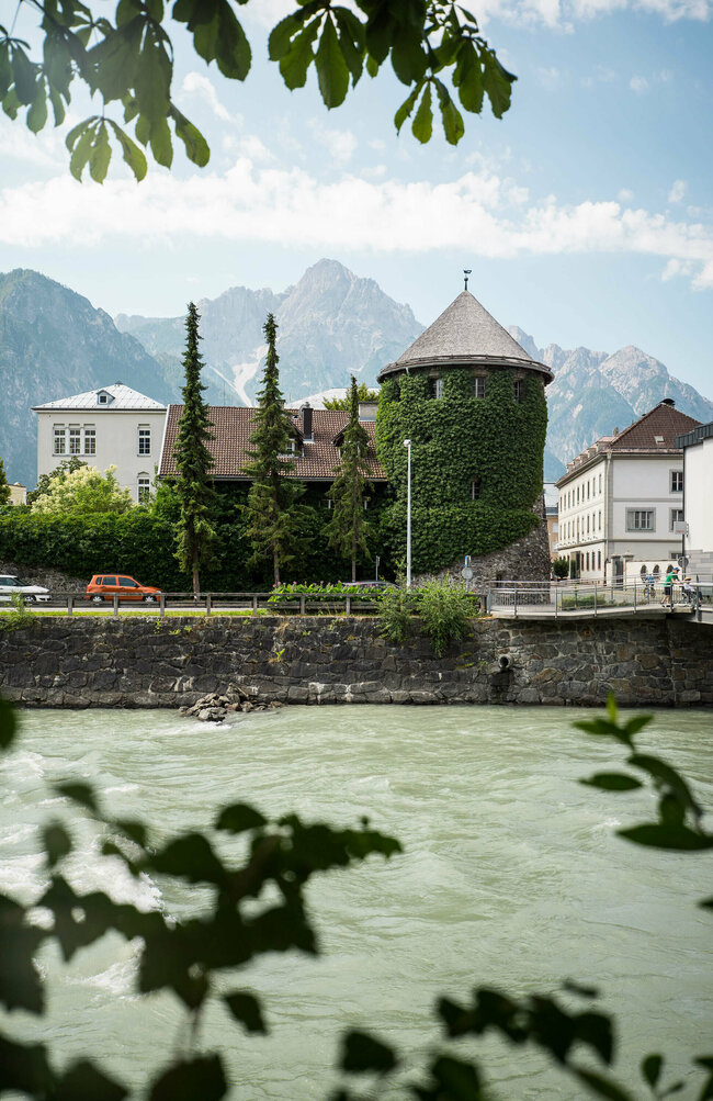 Blick von der anderen Flussseite auf den grün bewachsenen Iselturm in Lienz.