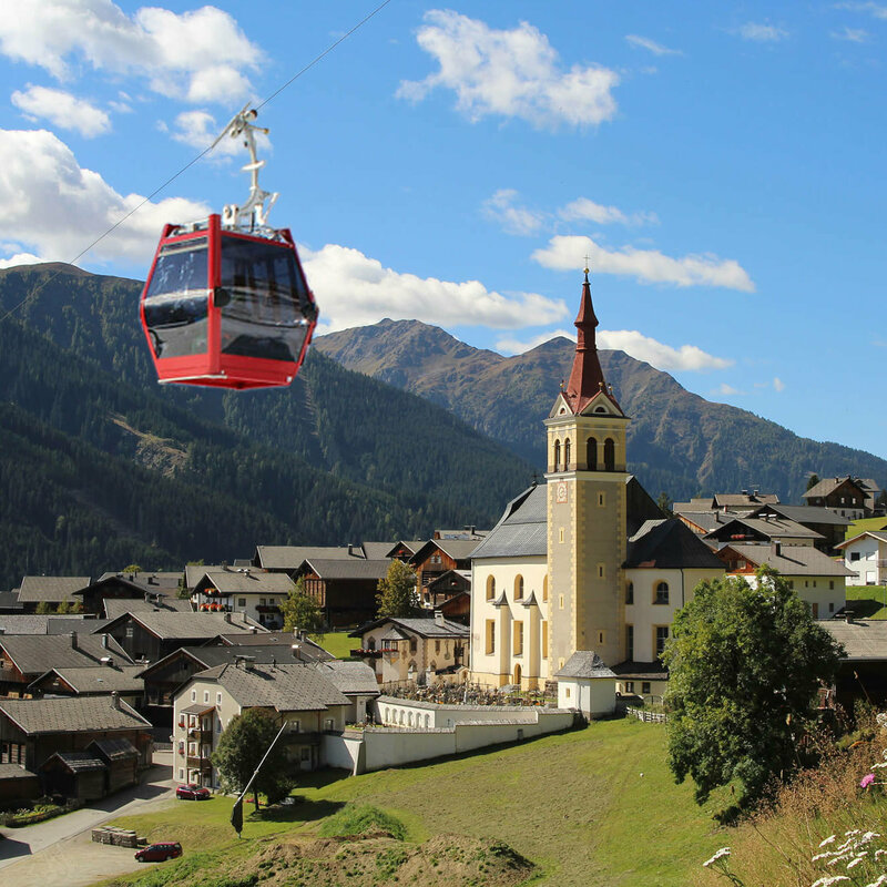 Sommergondel der Obertilliach Bergbahn fährt am Tal und der Kirche Obertilliachs vorbei