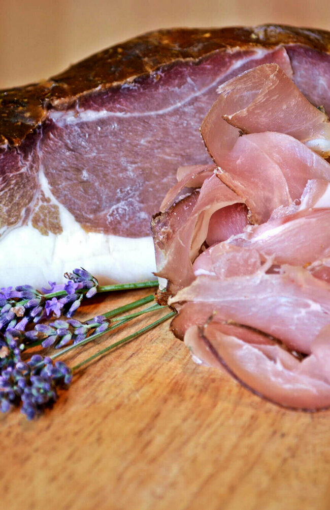 Ein großes Stück Speck mit ein paar dünnen Scheiben geschnittenem Speck und Lavendel.