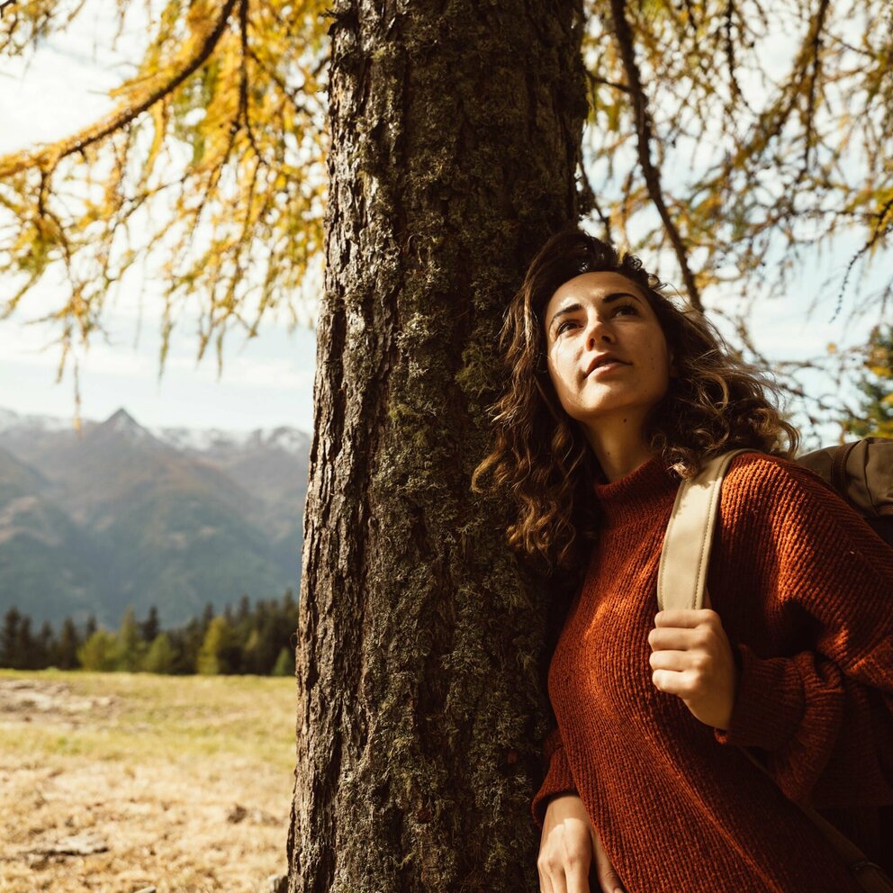 Wandern Zedlacher Paradies Frau lehnt sich im Zedlacher Paradies an einen vom Herbst gelb verfärbten Baum.
