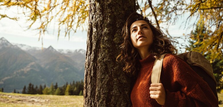 Frau lehnt sich im Zedlacher Paradies an einen vom Herbst gelb verfärbten Baum.