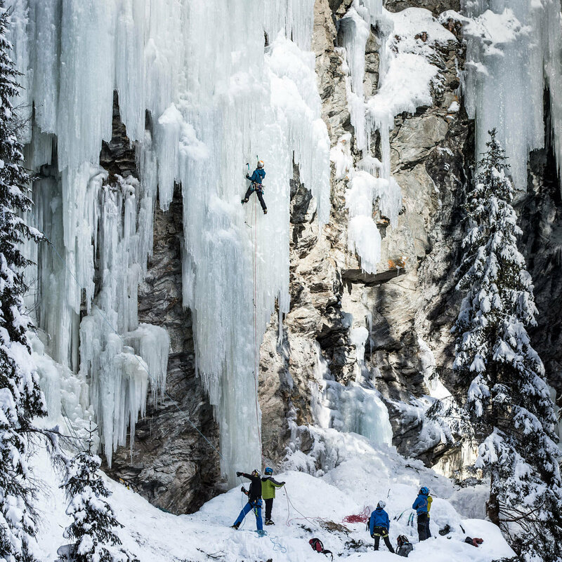 Auf einem gefrorenen Wasserfall klettern mehrere Menschen hoch