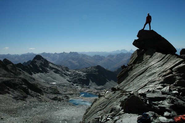 Ein Mensch steht auf einem Steinvorsprung mit Blick in die Berglandschaft und einem See.