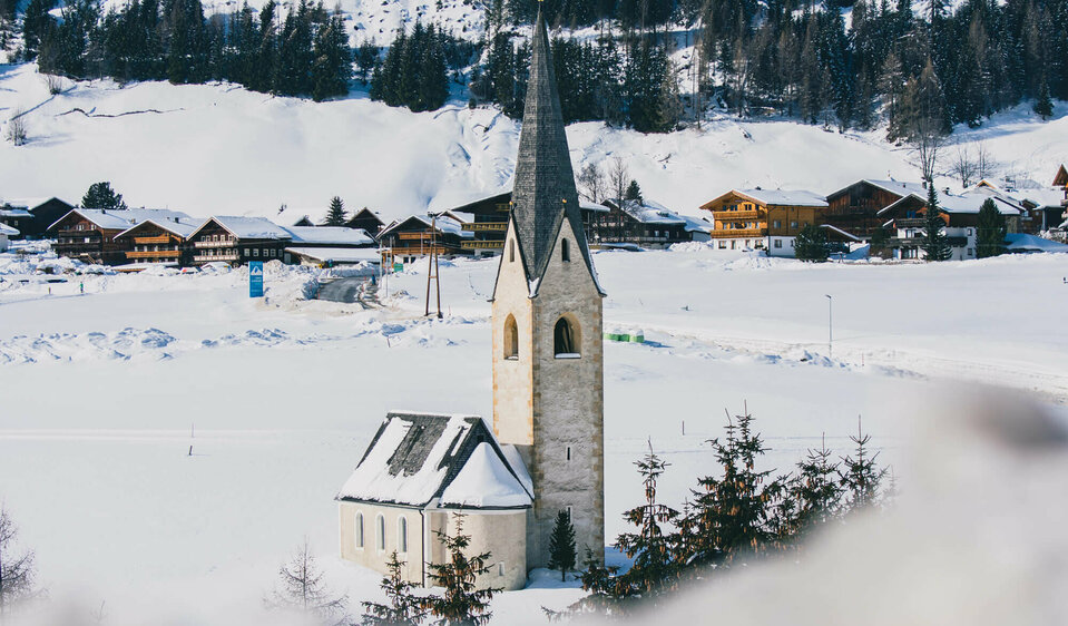 Die Kals Kirche mit dunklem Kirchturm liegt von Schnee bedeckt vor dem Dorf.