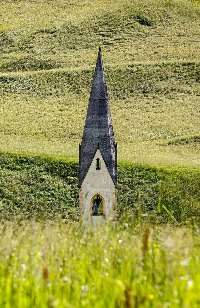 Blick auf eine Kirchturmspitze inmitten einer saftig grünen Bergwiese in Kals am Großglockner.