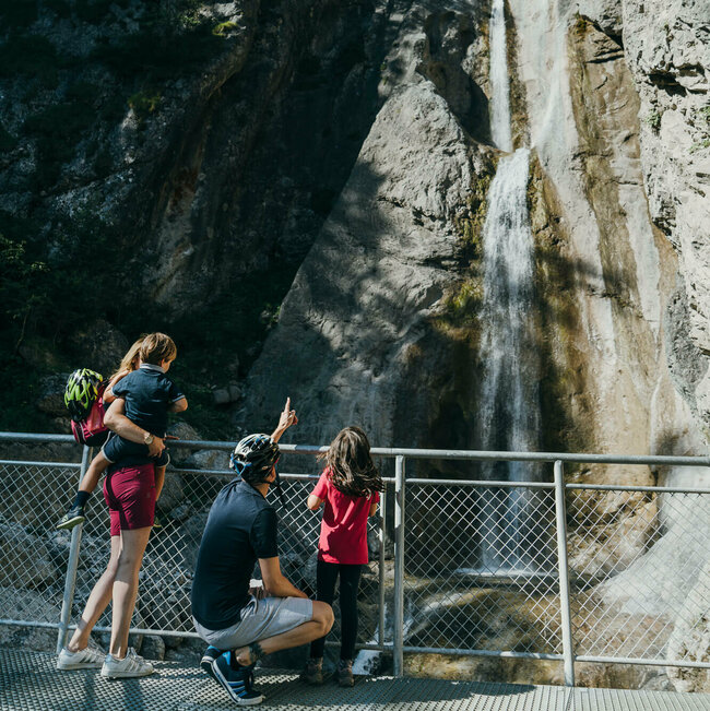 Eine vierköpfige Familie steht auf der Plattform des Frauenbachwasserfalls in Lavant. Ein Rundwanderweg, auch "Waldpfad" genannt, führt direkt an diesem Naturjuwel vorbei.