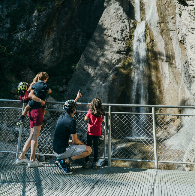 Eine vierköpfige Familie steht auf der Plattform des Frauenbachwasserfalls in Lavant. Ein Rundwanderweg, auch "Waldpfad" genannt, führt direkt an diesem Naturjuwel vorbei.