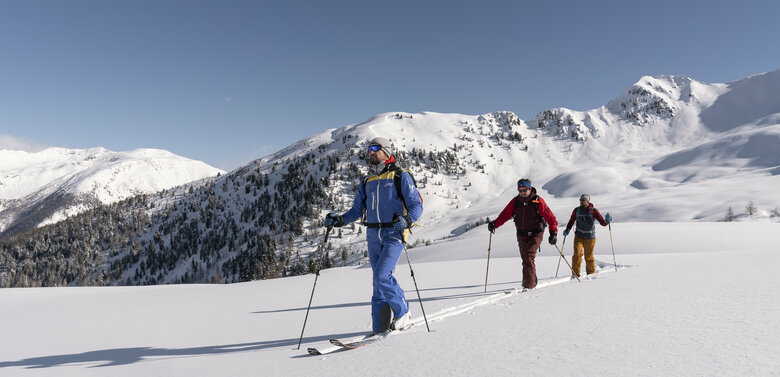 Drei Skitourengeher auf einem flachen Schneefeld in Villgraten bei wolkenlosem Himmel.