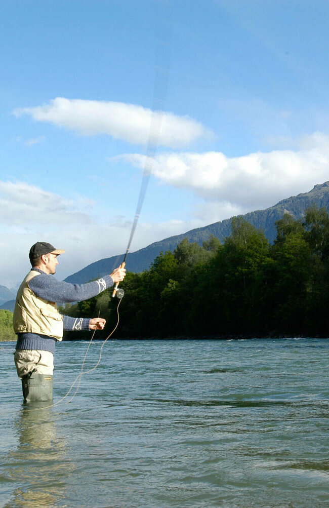 Fliegen fischen Ein Mann steht in einem Fluss und wirft seine Angel aus zum Fliegen fischen.