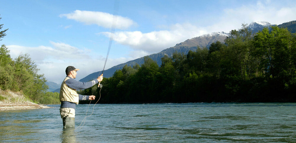 Ein Mann steht in einem Fluss und wirft seine Angel aus zum Fliegen fischen.