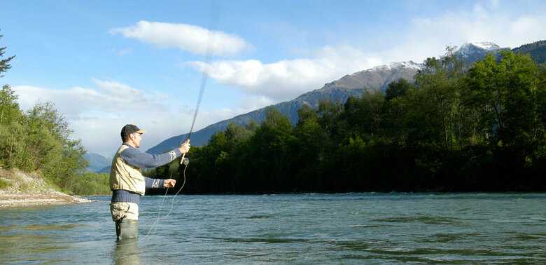Ein Mann steht in einem Fluss und wirft seine Angel aus zum Fliegen fischen.