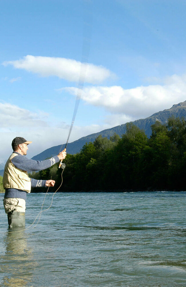 Fliegen fischen Ein Mann steht in einem Fluss und wirft seine Angel aus zum Fliegen fischen.