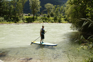Eine Person mit Schwimmweste und Helm steht auf einem Stand Up Paddle Board auf der Isel.