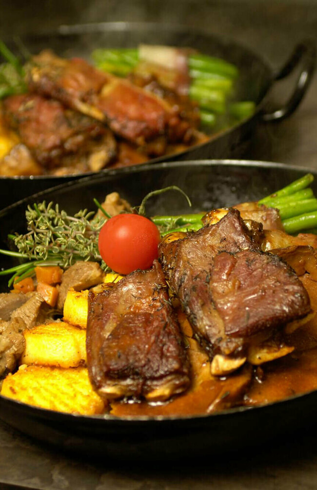 Osttiroler Berglamm mit Speckbohnen und Polenta in einem Eisenpfännchen.
