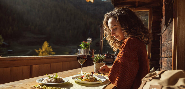 Eine Frau genießt eine Portion Schlipfkrapfen auf der Terasse der Unterstaller Alm