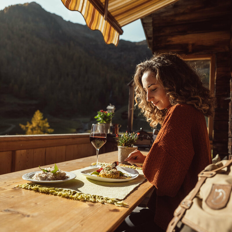 Eine Frau genießt eine Portion Schlipfkrapfen auf der Terasse der Unterstaller Alm